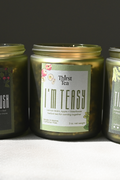 Three glass jars of Thirst Tea candles in a row on a light gray surface against a dark gray background. The label reads , 'I'M TEASY'